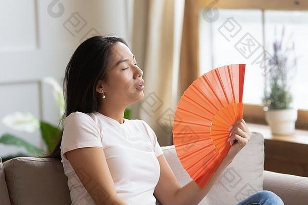 亚洲女人挥舞着风扇冷却热天气在室内