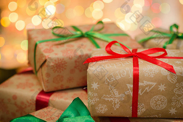 圣诞礼品<strong>盒</strong>包装在主题工艺纸和缎红色和绿结散焦圣诞灯背景空间，用于复制文本