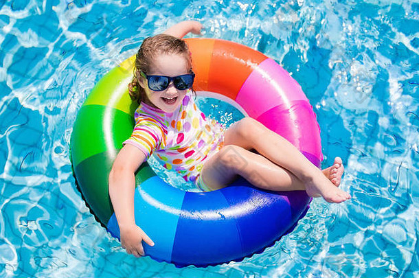 在炎热的夏日，快乐的小女孩在室外游泳池里玩着五颜六色的充气戒指。孩子们学习游泳。