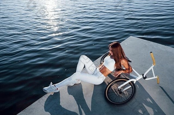 在自行车旁边。白天在湖边休息的健身妇女。美丽的阳光