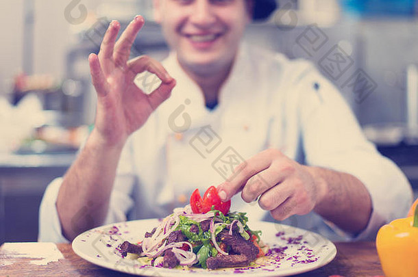 厨师长在餐厅商业厨房的盘子上装饰准备好的餐盘