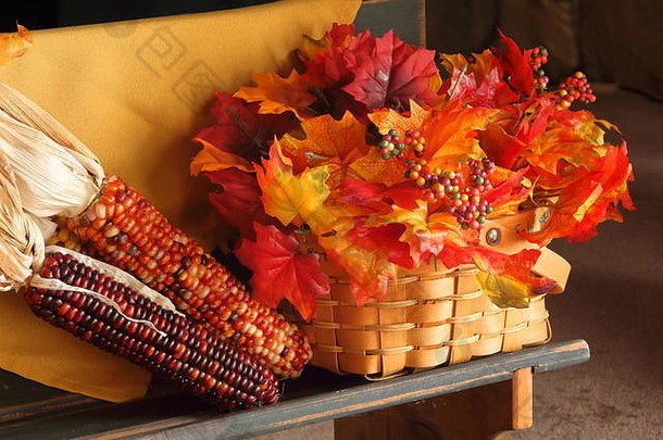 秋天的长凳上展示着树叶、南瓜和玉米，右侧有背景