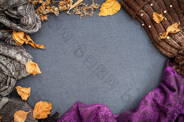 秋冬平躺。棕色针织小豆豆、紫色围巾和蓝色空白背景上的干树叶。