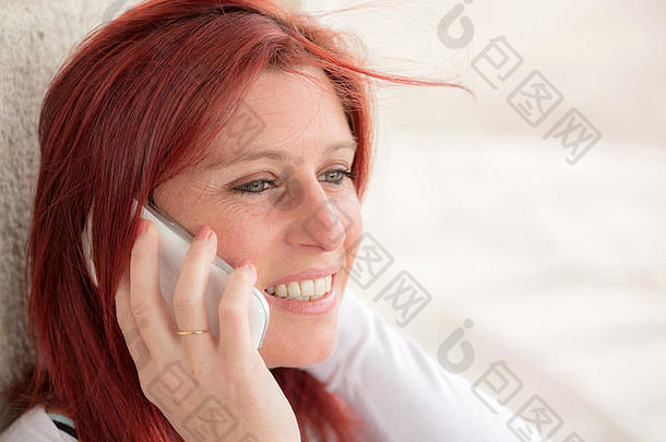 一位面带<strong>微笑</strong>的红发美女靠着一面旧墙用手机<strong>打电话</strong>
