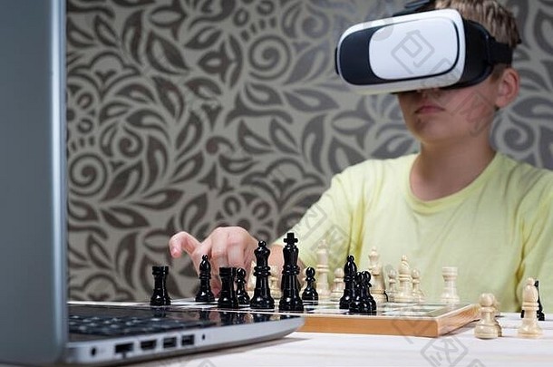 一个戴着虚拟现实耳机的男孩用笔记本电脑下棋。利用信息技术学习下棋