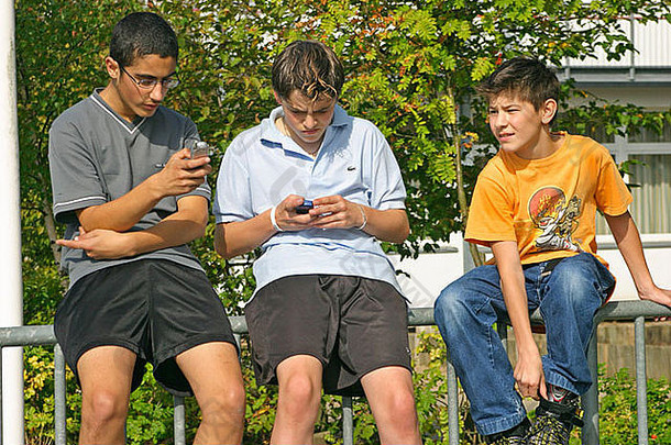 三个小男孩坐在篱笆上用手机