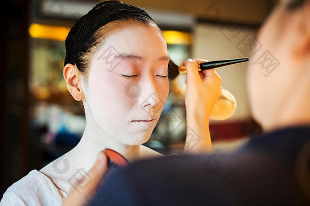一位现代艺妓或舞妓，以传统的方式准备，脸上涂着白色的化妆品。