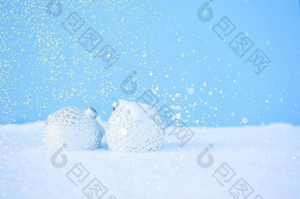 白色的圣诞球以美丽的图案躺在白色的雪地上，蓝色的背景上闪闪发光。圣诞节和新年的概念。