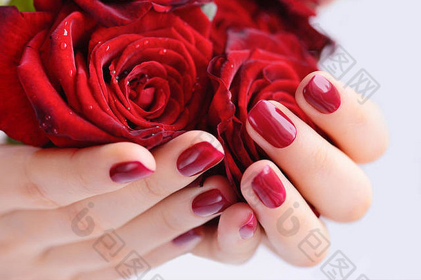 一位修过红指甲、手上插着一束红玫瑰的女士的手。闭合