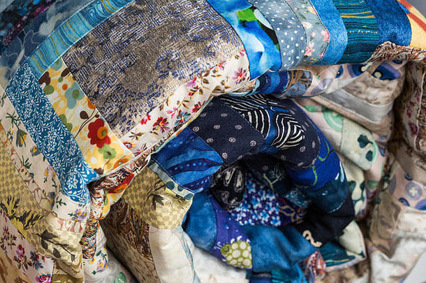 缝纫、拼贴和时尚概念-明亮的蓝色美丽多色绗缝毛毯卷在筒中，成品针线产品仓库，侧面视图。
