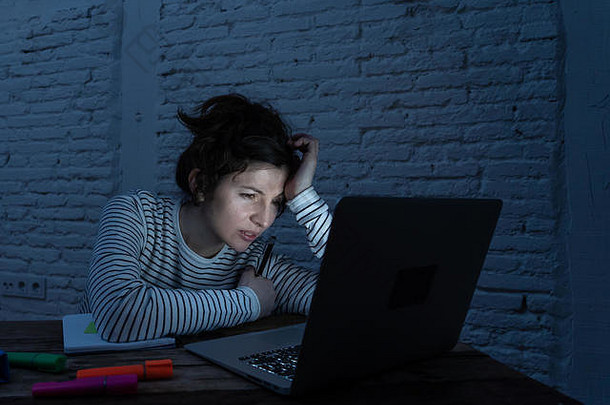 过度劳累的女学生深夜在笔记本电脑上工作，试图不入睡。感到疲劳，试图集中精力保持清醒