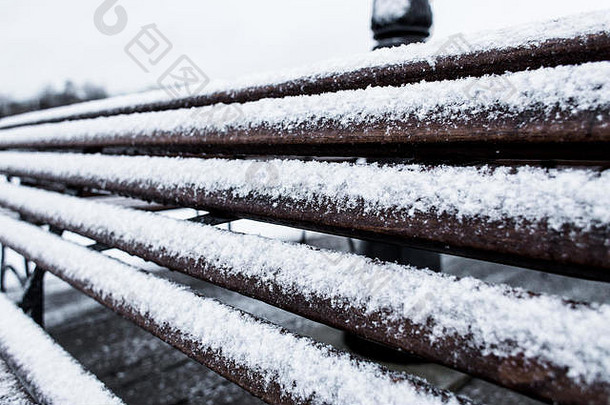 在多云的冬日，特写的冰冻长凳覆盖着粗砂粗糙的白霜