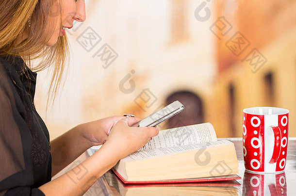 年轻的浅黑肤色的女人女人穿黑暗毛衣坐着紧迫的移动电话红色的杯子前面书说谎表格