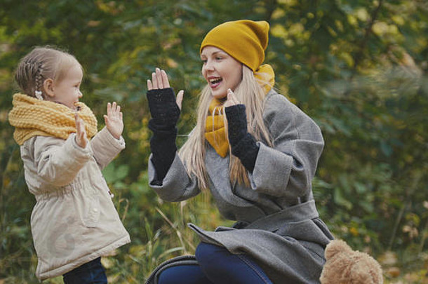 金发碧眼的小女孩和她的妈妈在秋天公园里度过了一段时间——玩耍、拍手、特写