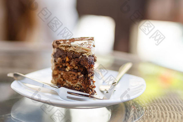 一块巧克力蛋糕放在盘子里，刀叉放在玻璃桌上