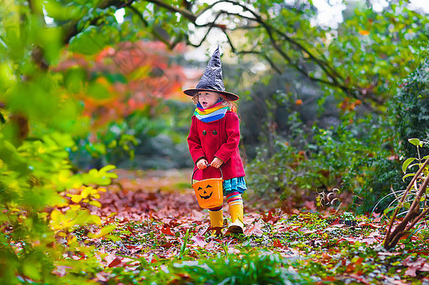 穿着女巫服装的小女孩在秋季公园玩耍。万圣节不给糖就捣蛋的孩子玩得很开心。孩子们不给糖就捣蛋。