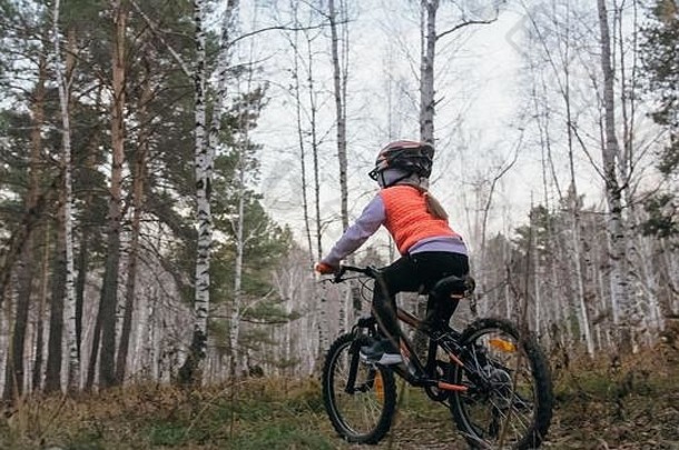 一名白人儿童在秋季公园骑自行车。小女孩在森林里骑着<strong>黑橙</strong>色的自行车。这孩子去做自行车运动。骑自行车的运动骑乘