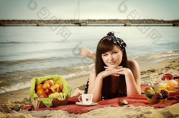 在户外野餐。美丽的女人躺在沙滩上的红毯子上。复古风格。