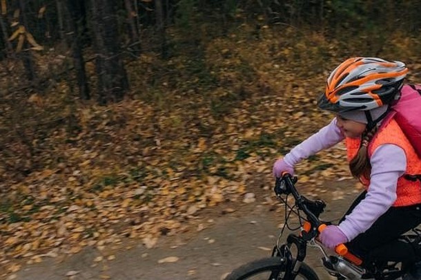 一名白人儿童在秋季公园骑自行车。小女孩在森林里骑着黑橙色的自行车。这孩子去做自行车运动。骑自行车的运动骑乘