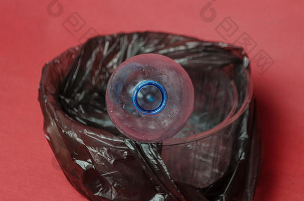 塑料透明空瓶，装在一个黑色袋子里，装在一个红色背景的容器里，并留有文本的空间。塑料对环境污染的概念