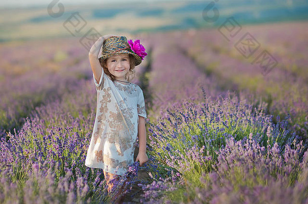 一个年轻漂亮的女孩穿着漂亮的衣服和帽子在周末的薰衣草地上散步