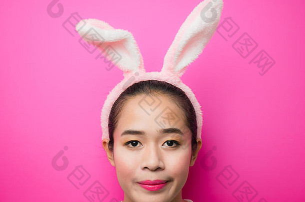 可爱的少女戴着兔子耳朵的头带和粉红色的背景。复活节期间戴兔耳头带的妇女。迷人的年轻女子和笑脸