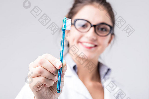 微笑女人白色实验室外套持有蓝色的塑料牙刷概念牙科口服卫生