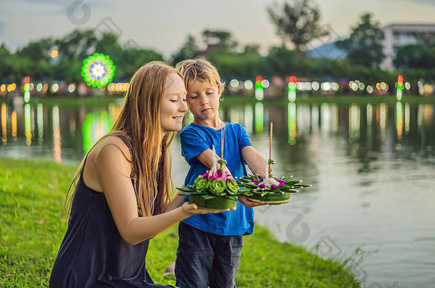 游客们的妈妈和儿子在水上跑步庆祝落水节。Loy Krathong节日，人们购买鲜花和蜡烛点燃，并漂浮在水面上