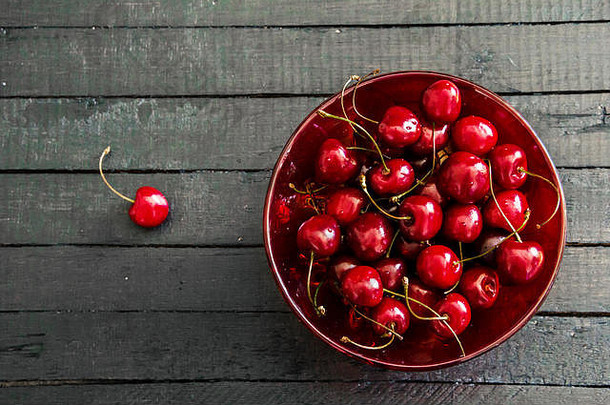 新鲜成熟的樱桃放在黑色木板桌<strong>子</strong>背景上的红色玻璃碗里。使用空间从上方查看