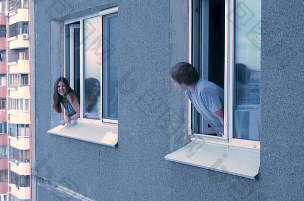 邻居们从窗口互相交谈。一对幸福的年轻夫妇在窗口聊天。邻居的概念。一对年轻夫妇一边聊天，一边隔着窗户看着对方