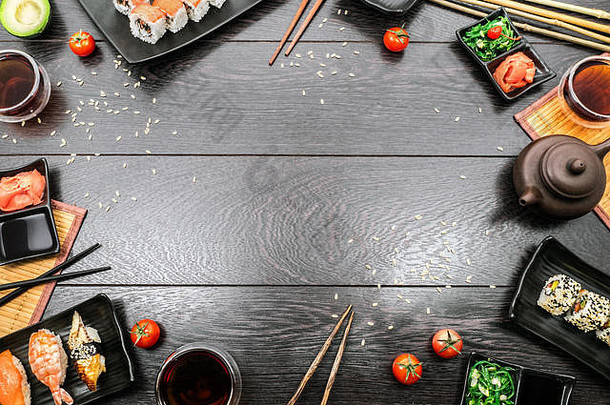 寿司套装生鱼片、尼吉里、马古罗和寿司卷放在盘子里，茶壶和西红柿放在深色木质背景上。文本的空间。
