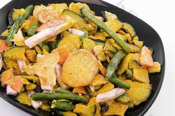 在一个黑色的碗里烤蔬菜片，包括红薯、青豆、芋头和<strong>南瓜</strong>。白色的隔离带。