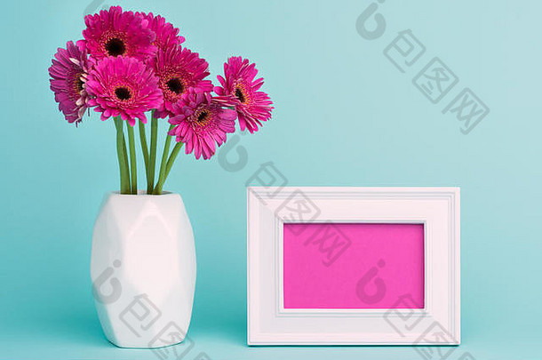 母亲节、妇女节、情人节或生日快乐彩色背景。桌子上花瓶里的粉红色非洲菊，画框是空的。