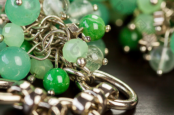 一件银色珠宝上漂亮的半透明绿色珠子的特写镜头，通过浅自由度的短链以时尚的概念连接在一个戒指上