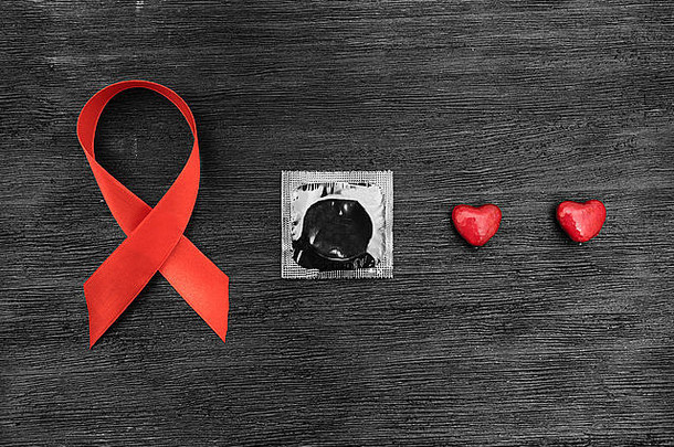 黑色背景上的艾滋病丝带、避孕套和心脏
