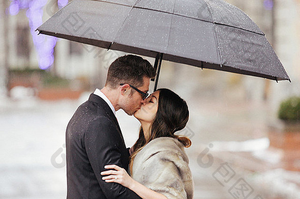 一对穿着晚礼服的夫妇，一男一女在伞下接吻