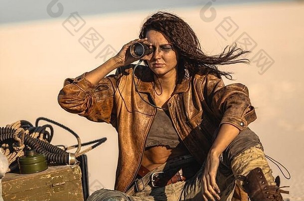 带着双筒望远镜的后世界末日英雄女人。背景是沙漠和死寂的荒地。穿着破旧衣服坐在营地里的英勇女战士。世界末日后的生活概念。