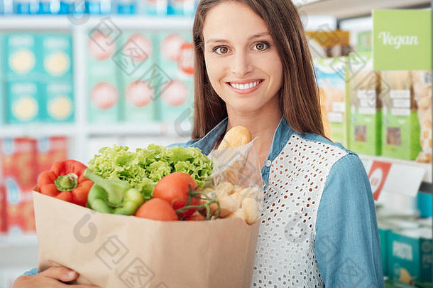 年轻微笑的女士在超市购买素食和新鲜蔬菜，健康饮食和购物理念