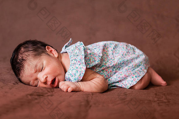 可爱的两周大的新生穿着花裙子，以胎儿的姿势安详地睡在床上/新生婴儿可爱的睡着了