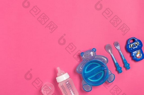 婴儿奶瓶和蓝色盘子，汤匙和叉子分开放在粉红色的盘子上。俯视图