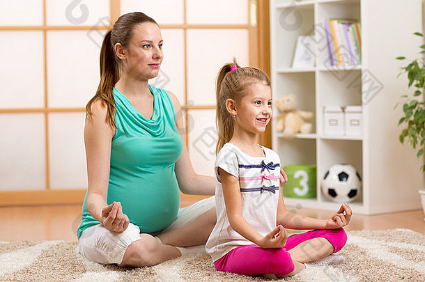 怀孕的母亲和孩子做瑜伽，在家里的健身垫上以莲花的姿势放松