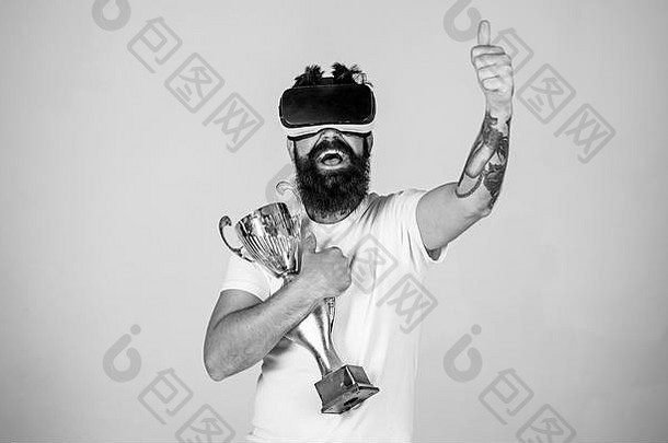 的家伙头安装显示赢得了虚拟游戏男人。胡子虚拟现实眼镜持有金杯状光背景赢家概念赶时髦的人快乐脸提高手拇指
