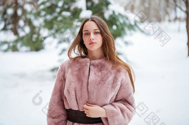 年轻漂亮的黑发女子穿着毛皮大衣在冬季公园摆姿势。模特穿着时尚保暖的衣服。