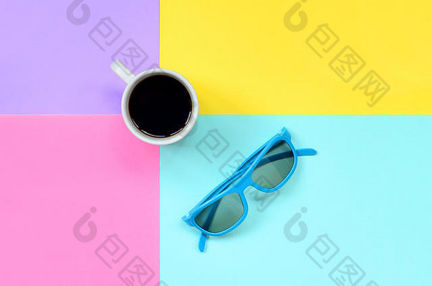 小型白色咖啡杯和蓝色太阳镜，以时尚柔和的蓝色、黄色、紫罗兰色和粉色纸为纹理背景，简约概念。