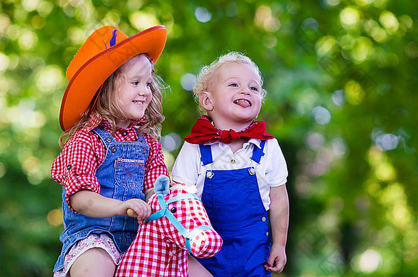 小男孩和小女孩装扮成牛仔和牛仔女孩，在公园里玩玩具摇马。孩子们在户外玩耍。