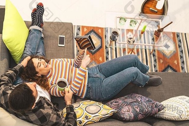 在家里沙发上休息时使用平板电脑的幸福情侣——年轻浪漫的情侣们享受新潮流科技设备带来的乐趣