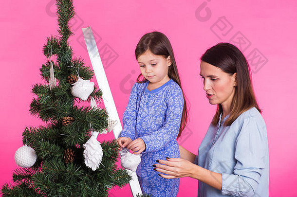 年轻的妈妈和她的女儿戴着粉红色背景的圣诞树