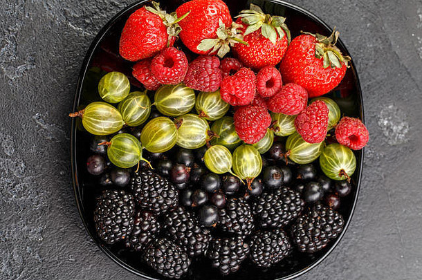 图为黑盘子上的黑莓、草莓、覆盆子、醋栗