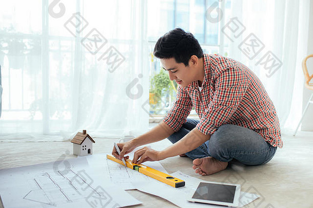 年轻英俊的亚洲男建筑师在家里的地板上工作。
