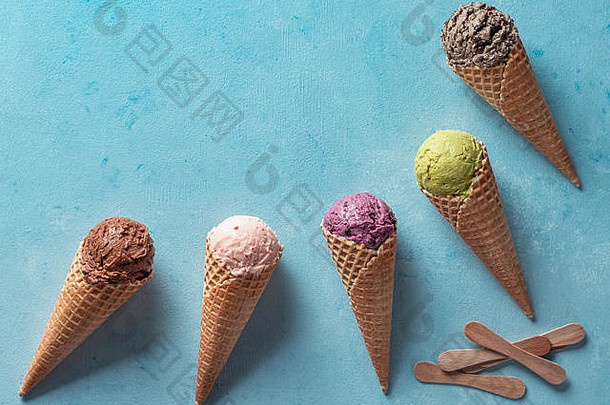 各种各样的<strong>冰淇淋</strong>舀在有空间的蛋筒里。彩色蛋卷<strong>冰淇淋</strong>巧克力，草莓，<strong>蓝莓</strong>，开心果或抹茶，饼干巧克力三明治饼干蓝色背景。俯视图